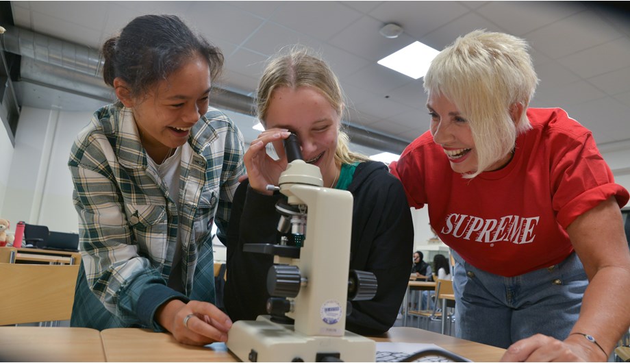 Leerlingen bekijken door een microscoop een preparaat. De docent helpt hen daarbij. 