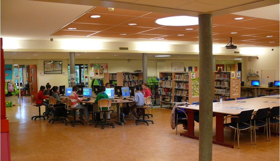 Onze multifunctionele ruimte met werkplekken, een computereiland én een schoolbibliotheek.
